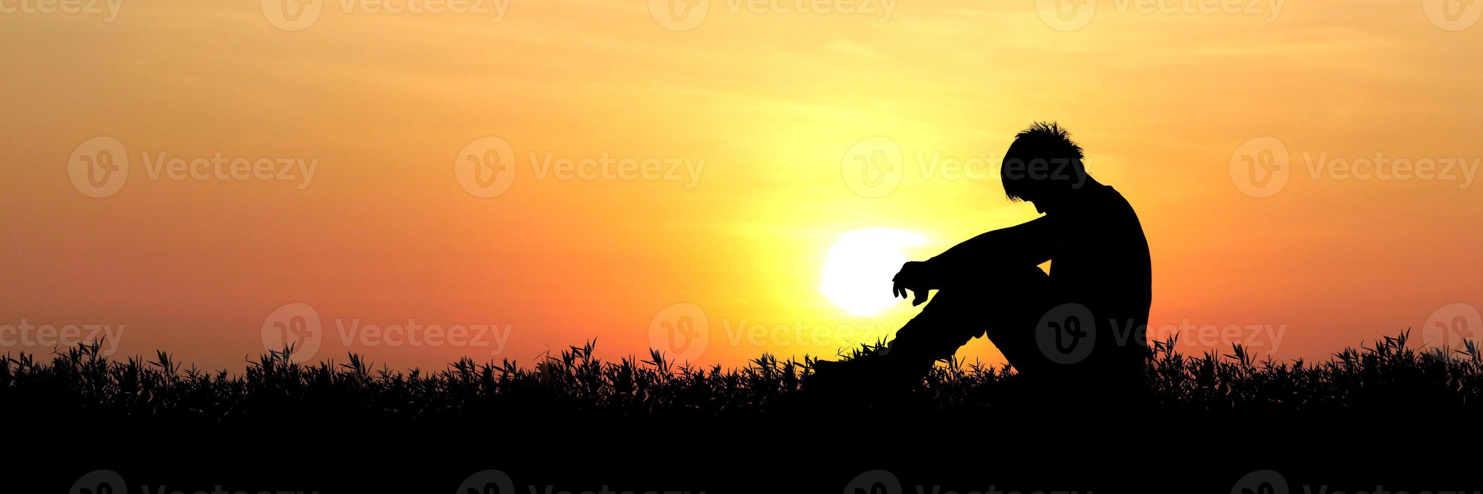 Silhouette of a Person Sitting in a Field at Sunset with a Vibrant Orange Sky photo