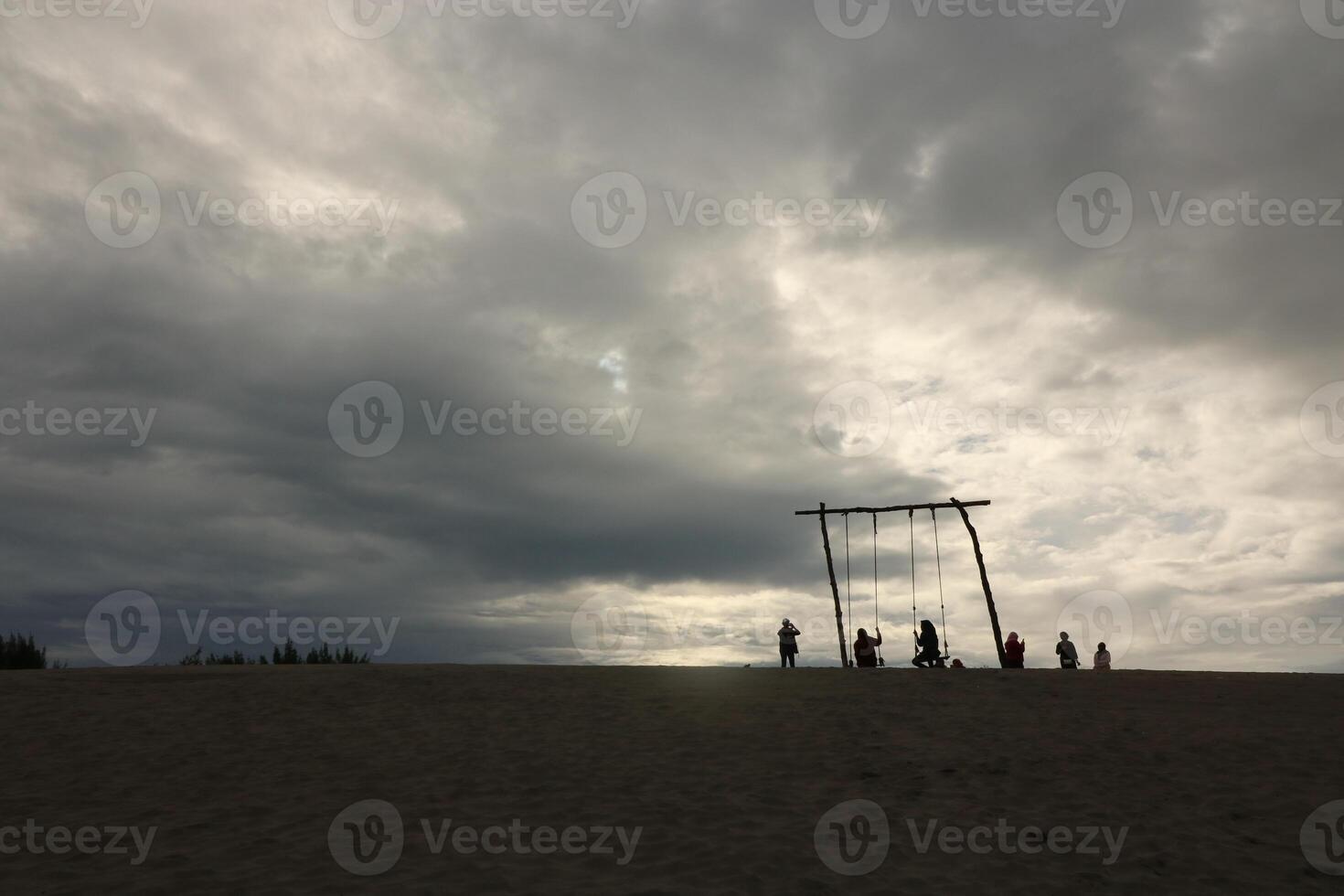 A Silhouette Group Of People Are Standing On The Beach And One Is Wearing A White Shirt photo