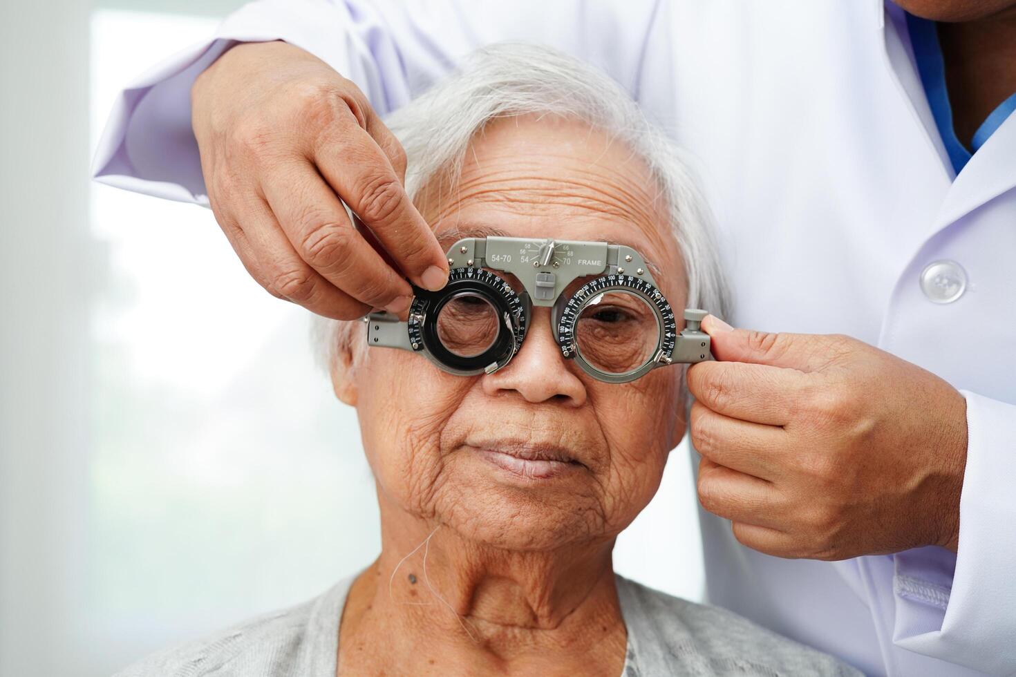 Optometrist checking Asian elderly woman ophthalmic vision eye test and using optical trial frame. photo