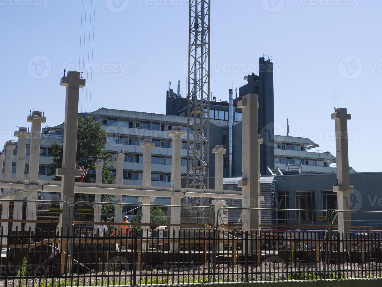Construction site with building being built, cranes in background. Workers and crane collaborate on building project. framework of building visible, showing active construction efforts. photo