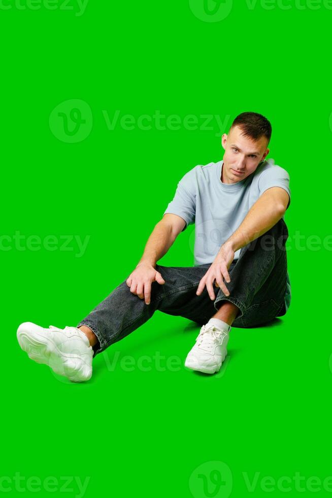 Casual Young Man Sitting on Floor in Comfortable Clothes With Green Background photo