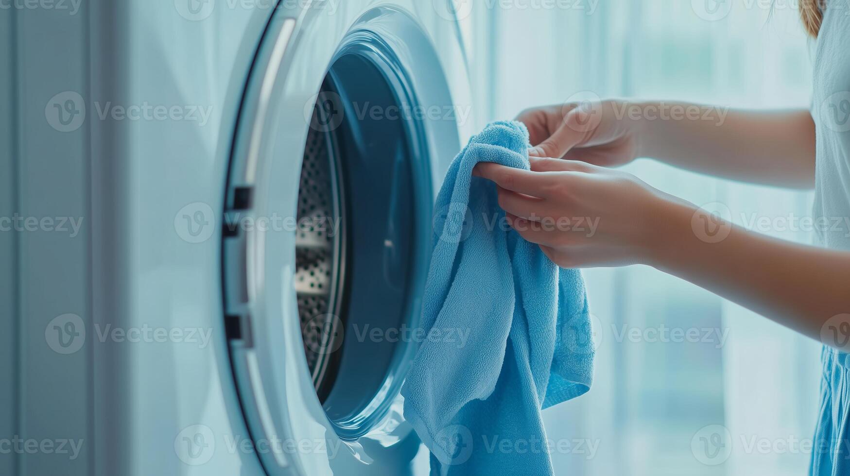 A person transferring freshly laundered blue fabric from a washing machine to a dryer in a modern laundry room during daylight hours photo