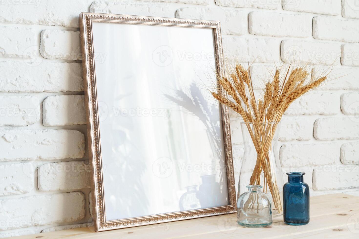 Vase with ears of wheat and photo frames against brick wall