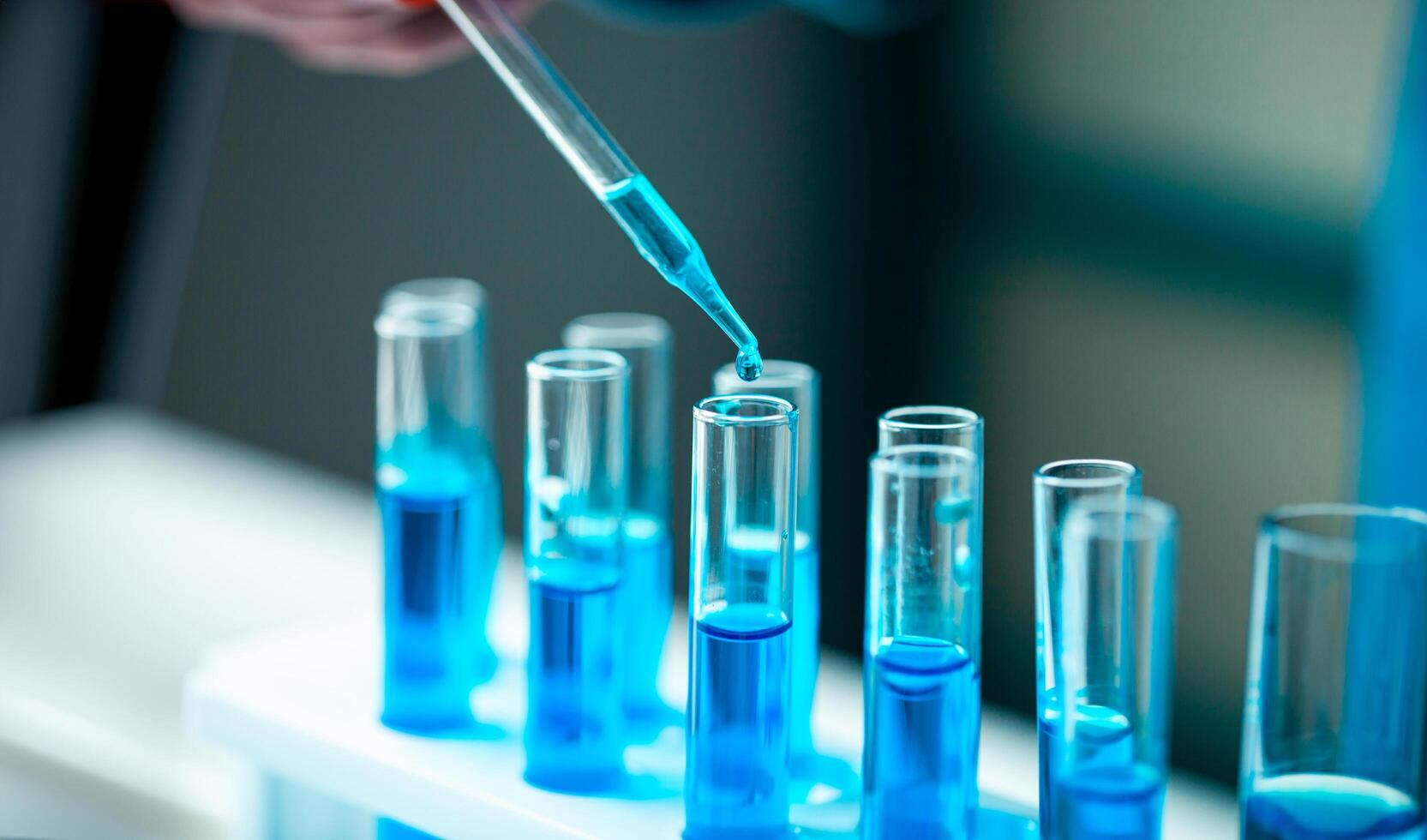 A person is pouring blue liquid into a row of test tubes photo