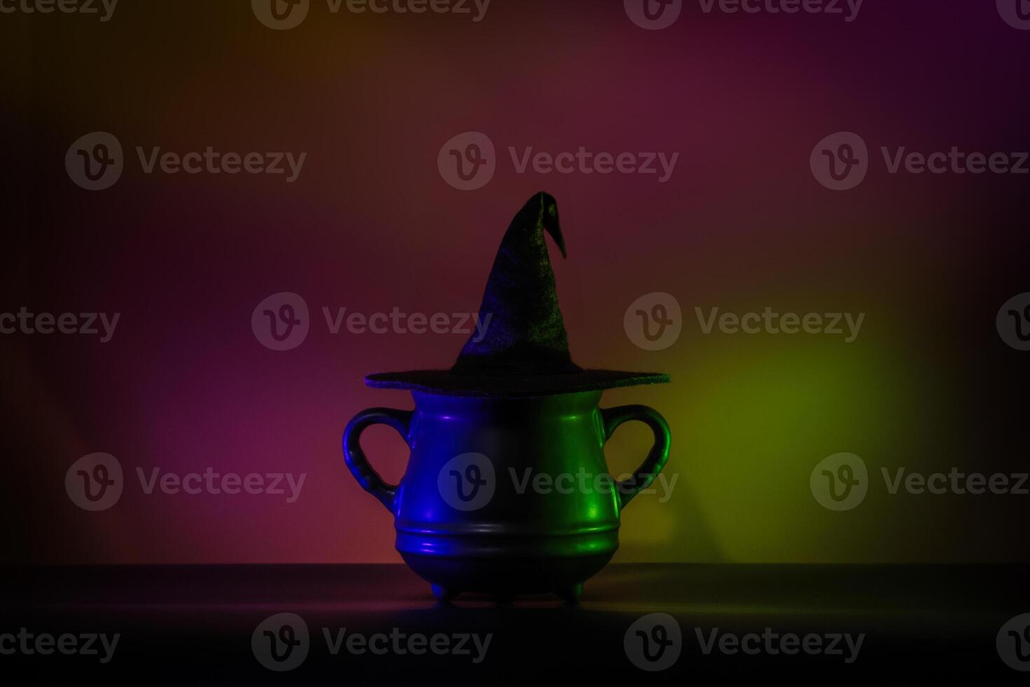 Creative minimalist Halloween background image featuring a witch hat on a cauldron in lowkey neon lighting. Perfect for modern and trendy Halloween designs. photo
