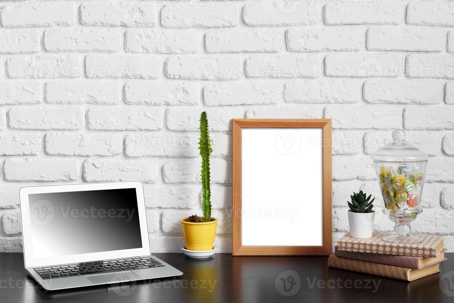 Worktable with laptop, stationery and decorations in home office with blank photo frame