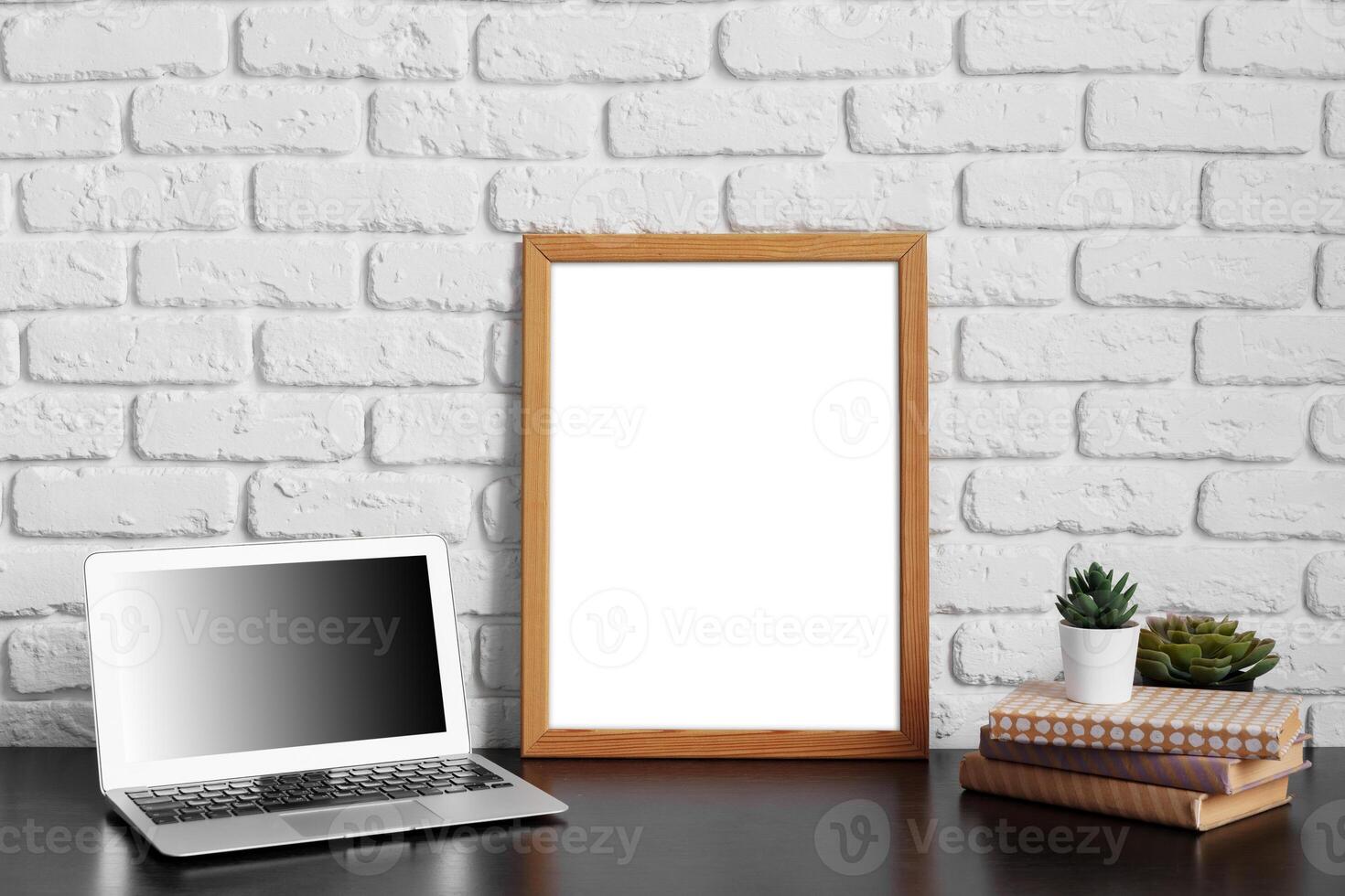 Worktable with laptop, stationery and decorations in home office with blank photo frame