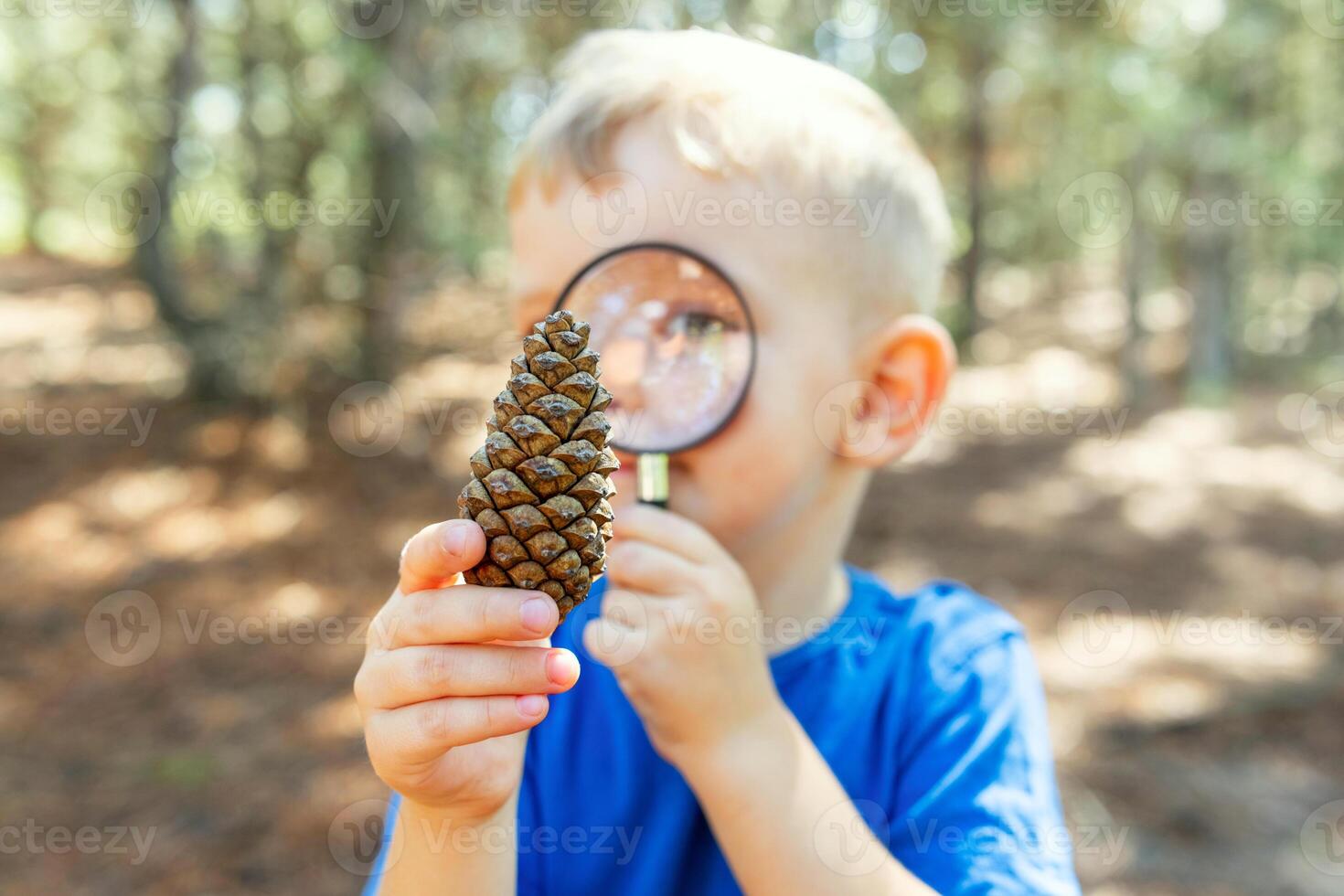 Curious boy is exploring nature with magnifying glass outdoors photo