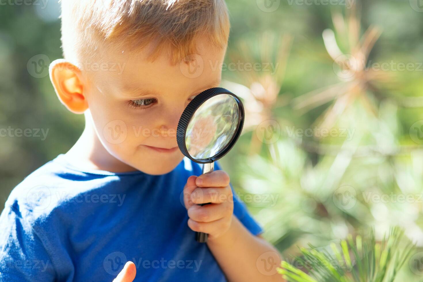 Curious boy is exploring nature with magnifying glass outdoors photo