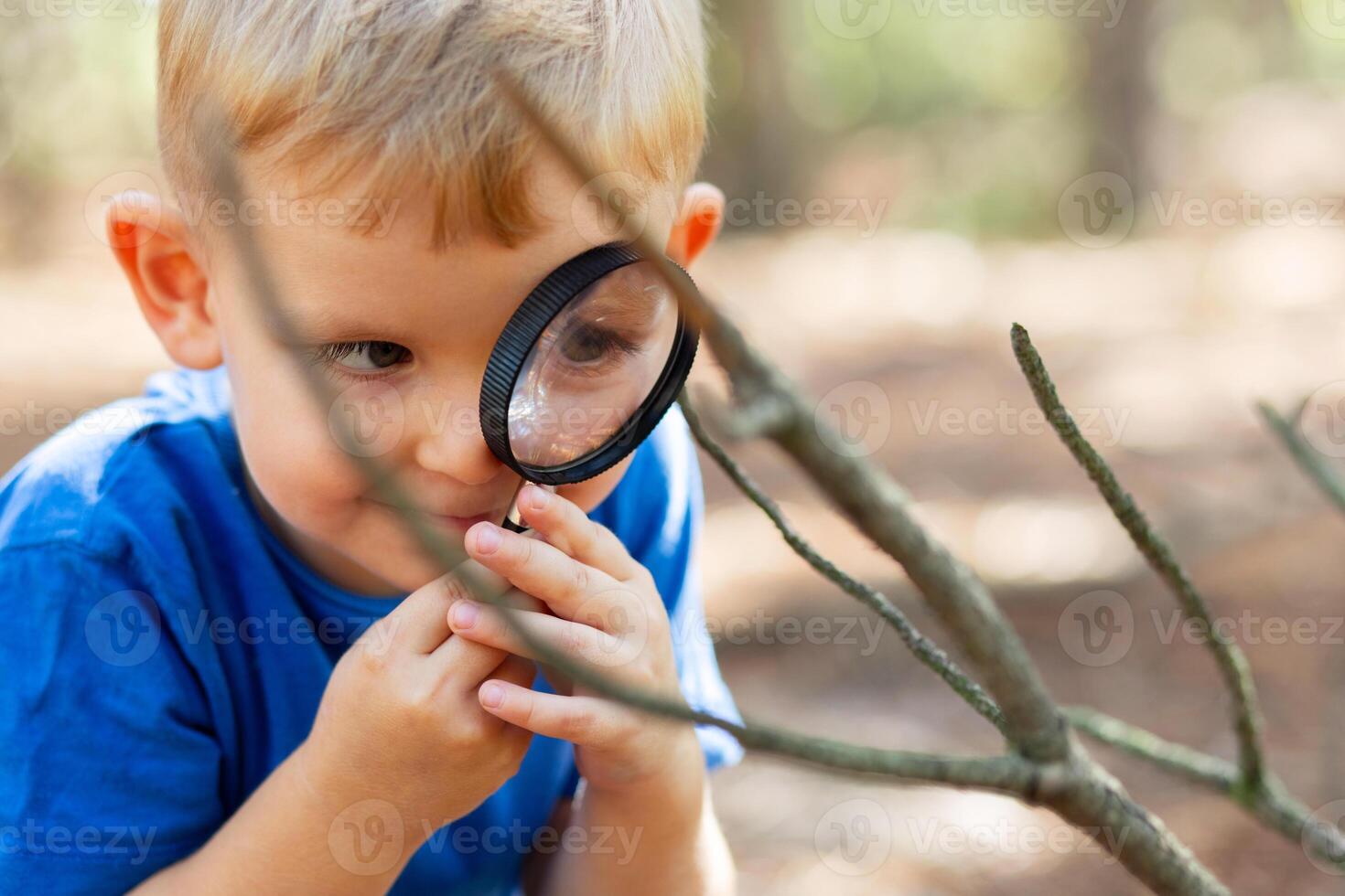 Curious boy is exploring nature with magnifying glass outdoors photo