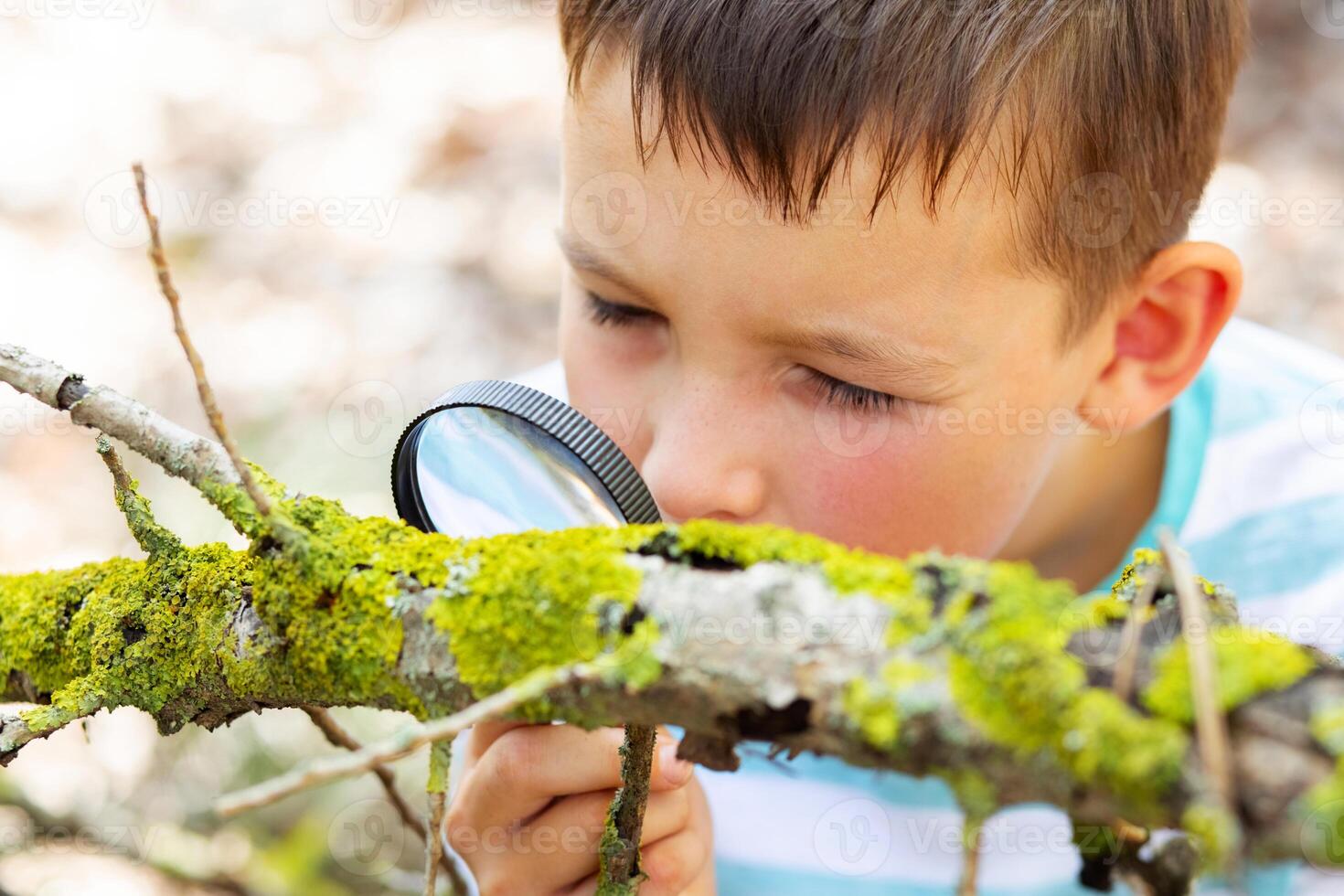 Curious boy is exploring nature with magnifying glass outdoors photo