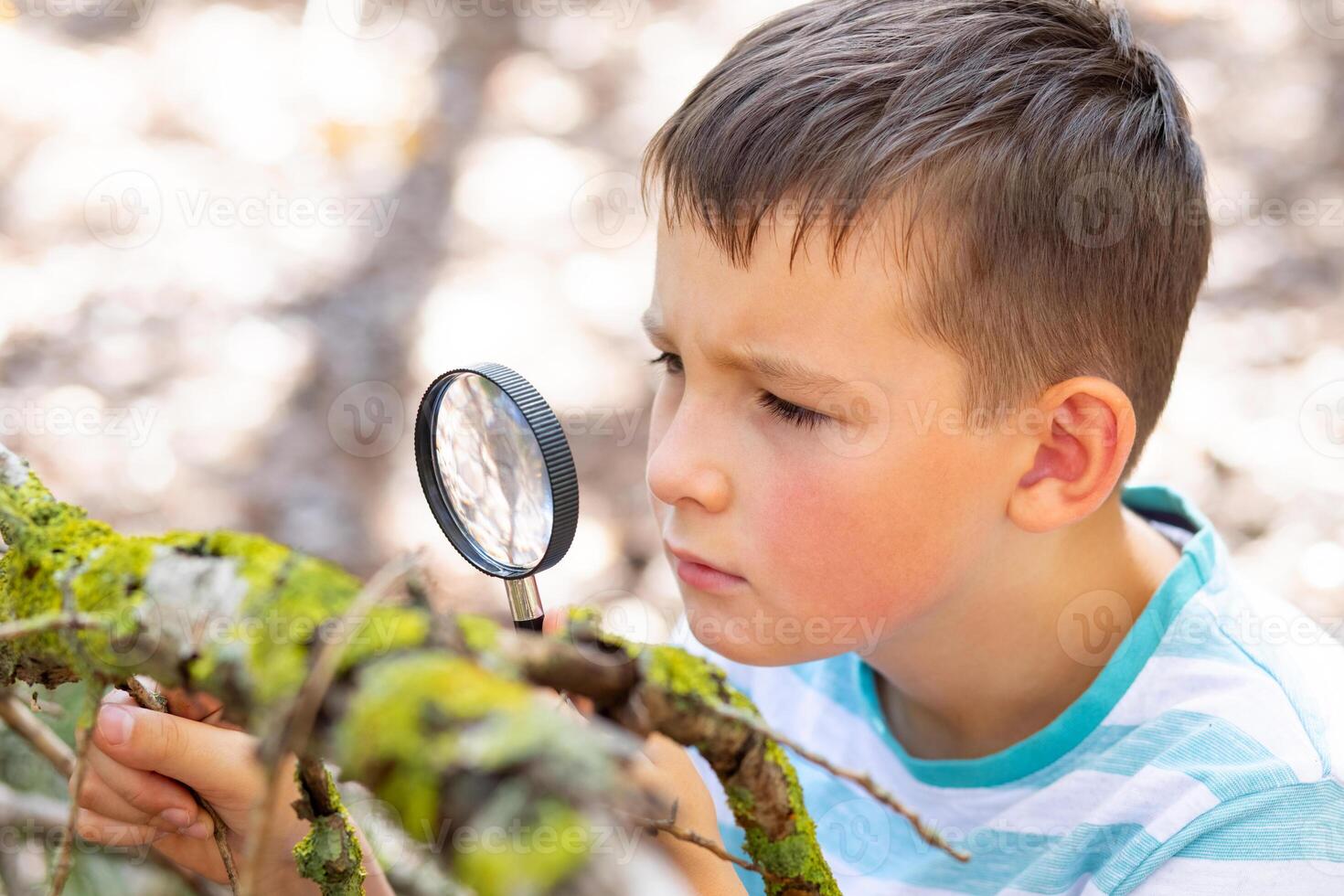 Curious boy is exploring nature with magnifying glass outdoors photo