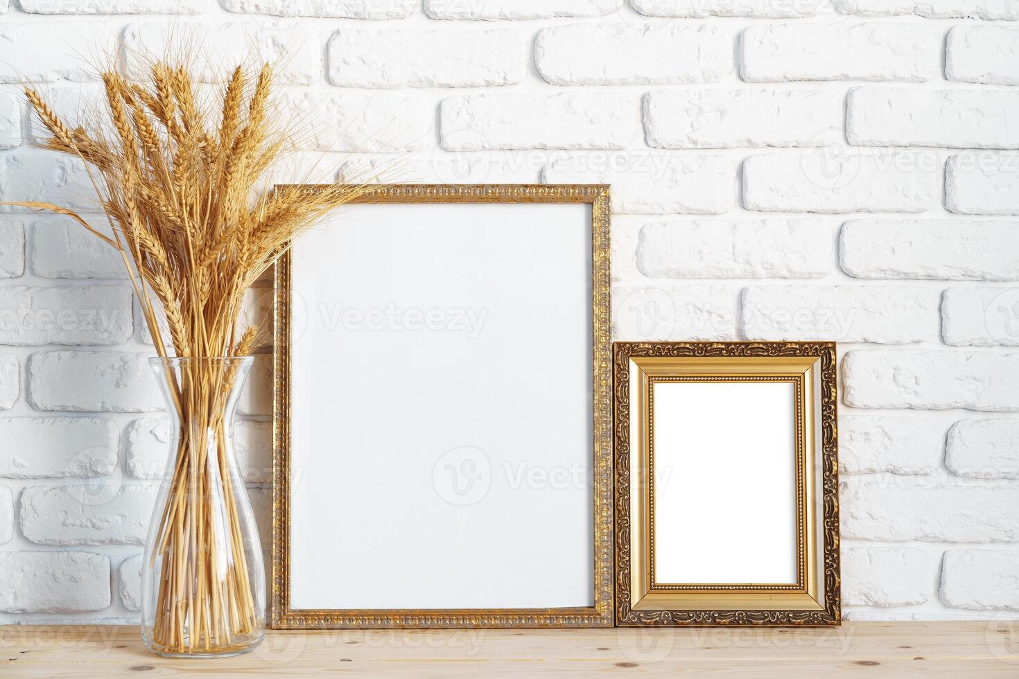 Vase with ears of wheat and photo frames against brick wall
