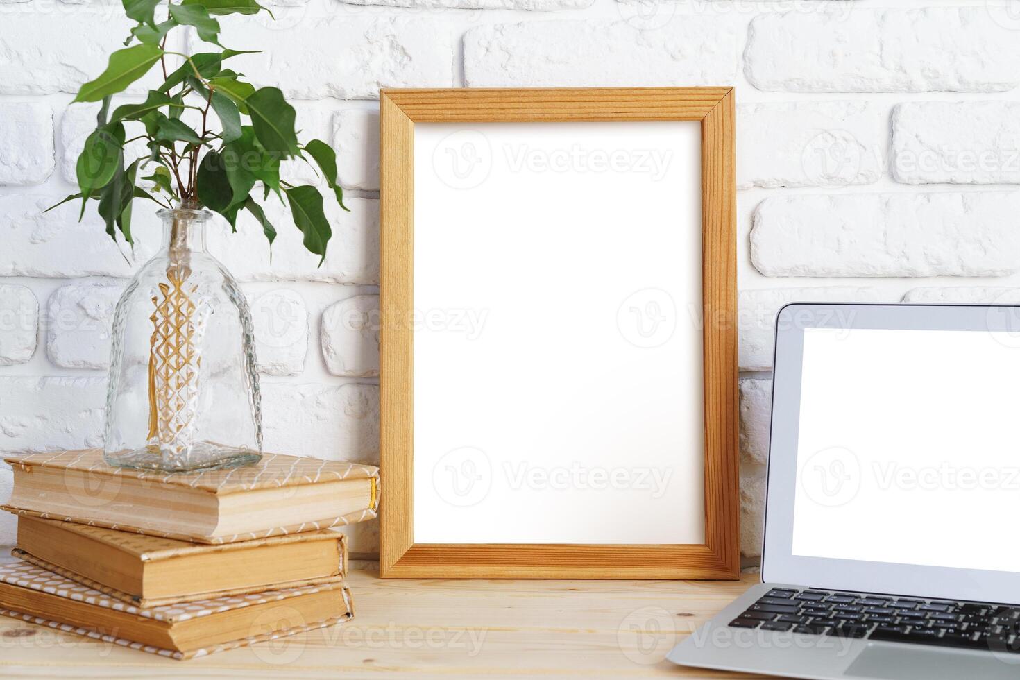 Blank picture frame on wooden table with books and laptop photo