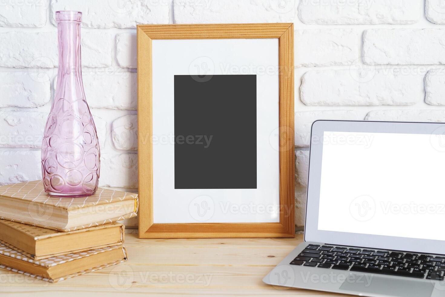 Blank picture frame on wooden table with books and laptop photo