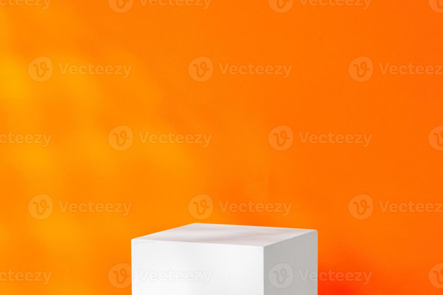 A white cube placed on a table against a vibrant orange wal photo