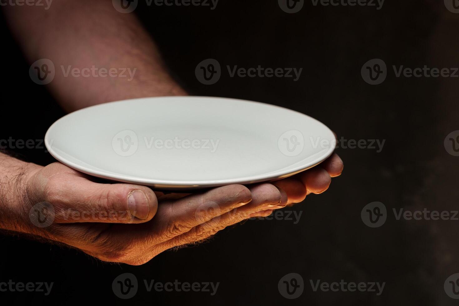 Male hands holding empty plate on dark background, lack of food, hunger concept. photo