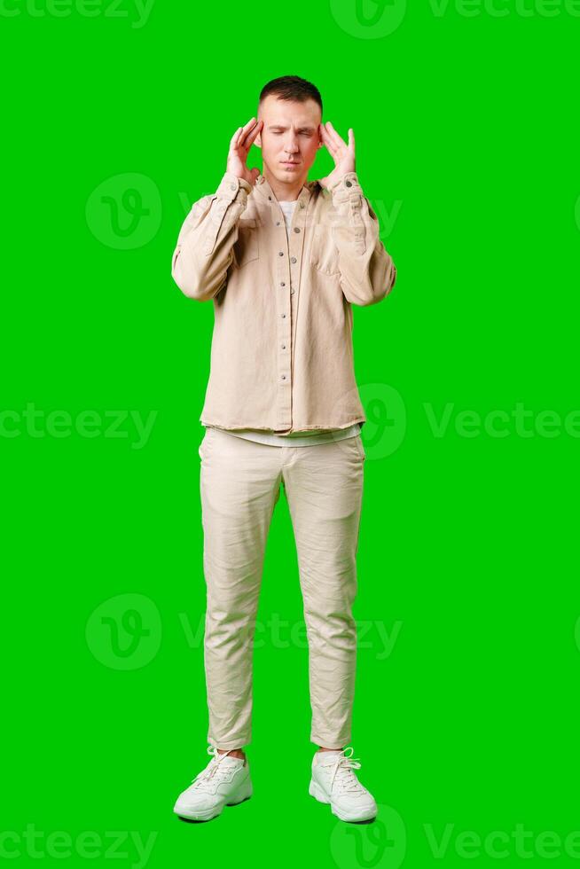 Man With Short Hair Wearing Beige Jacket Holding His Head in Frustration Against a Bright Green Background photo