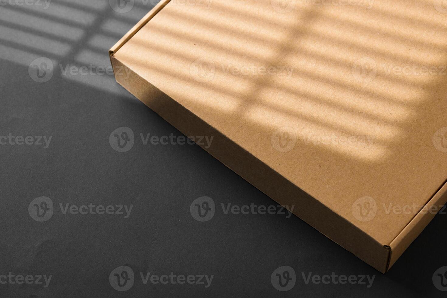 A cardboard box casting shadows on a dark surface in a striped light pattern photo