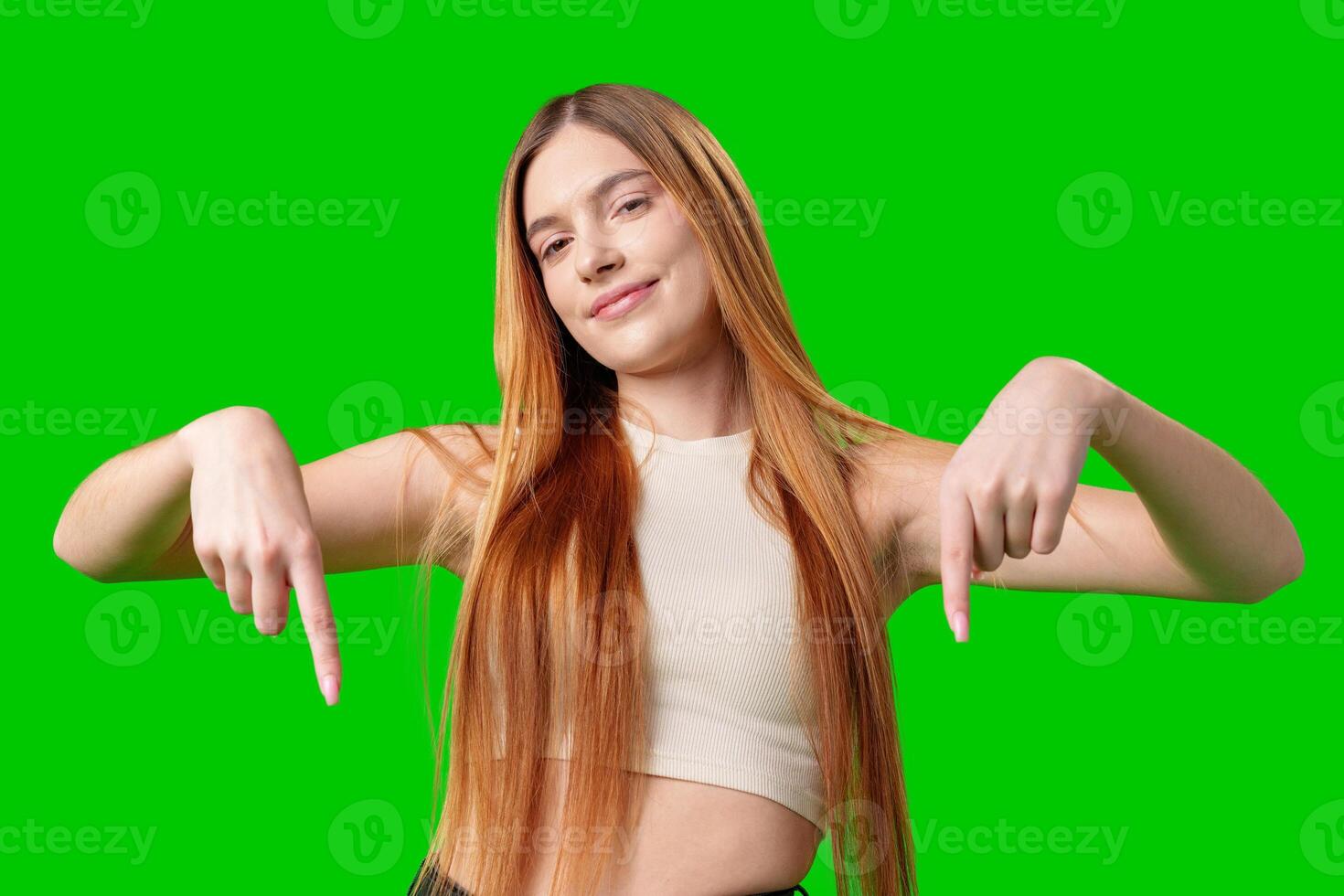 Young Woman Pointing Downwards in Front of Green Screen photo