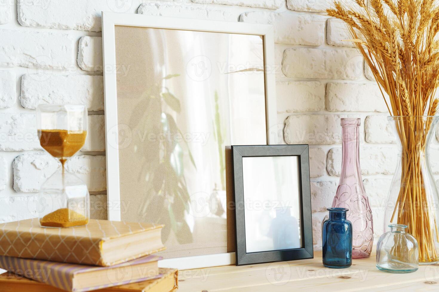 Vase with ears of wheat and photo frames against brick wall