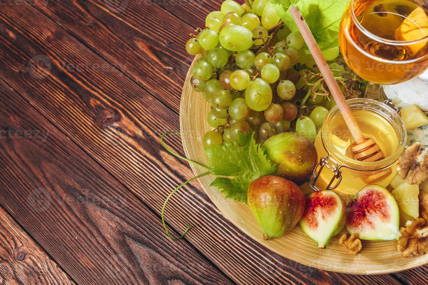 Grape, cheese, figs and honey with wine on wooden table photo