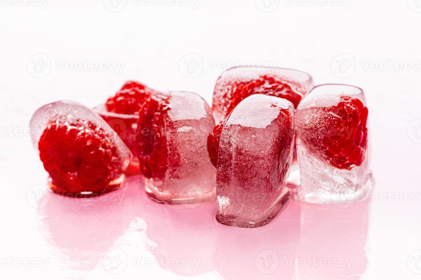 Raspberry ice cubes on pink glossy background photo