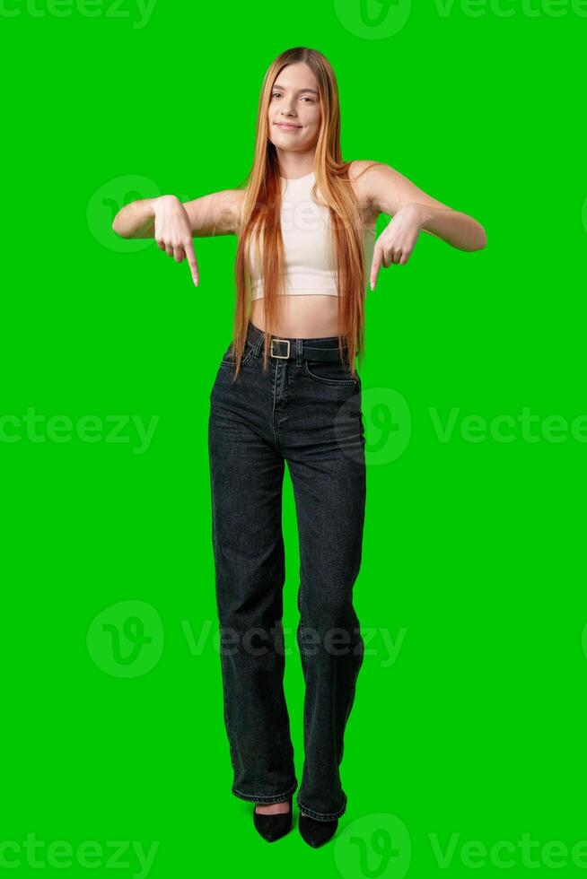 Young Woman Pointing Downwards in Front of Green Screen photo