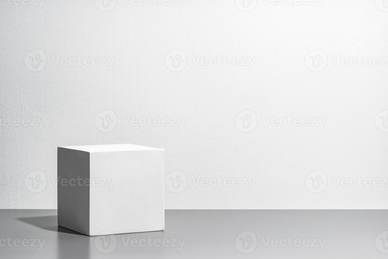 A simple white cube on a gray surface against a blank wall photo
