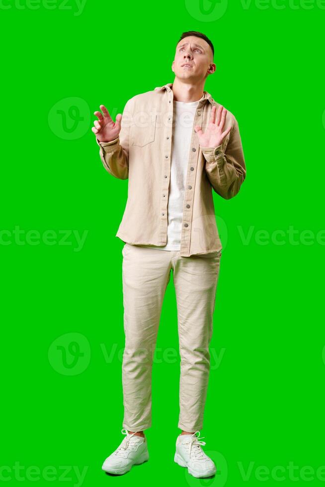 Man Wearing Casual Beige Outfit Poses Playfully Against Bright Green Background photo