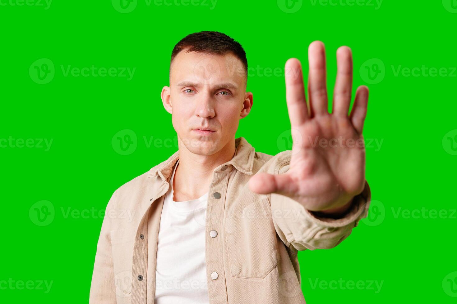 Man Holding Up Hand Against Bright Green Background While Displaying Serious Expression photo