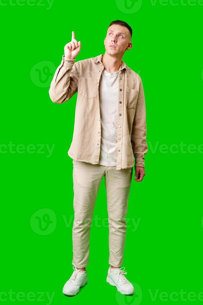Young Man Pointing Upward While Smiling Against a Bright Green Background photo