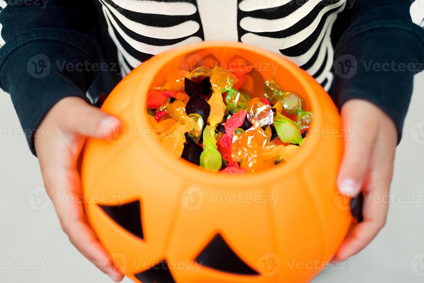 Little child holding full pumpkin bucket of candies on halloween party, playing tradition game trick or treat photo