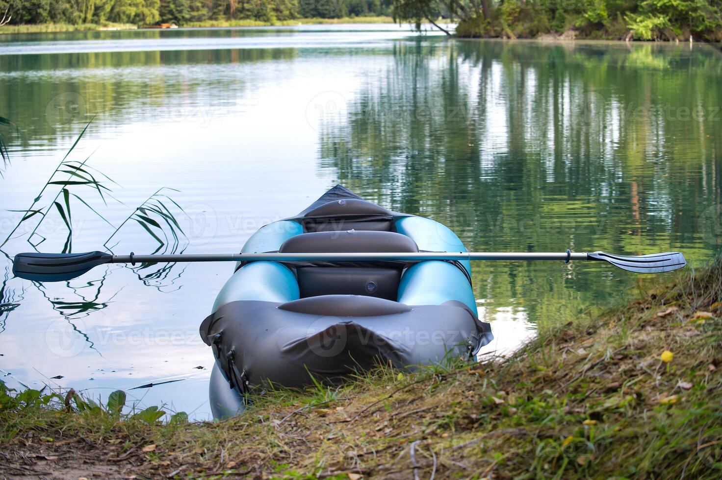 Tranquil scene of an inflatable kayak with a paddle on a lake shore photo