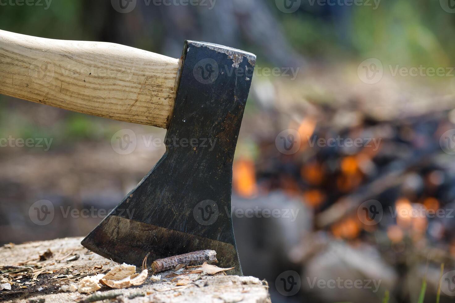 Close-up of an axe embedded in a log with a campfire burning in the background photo