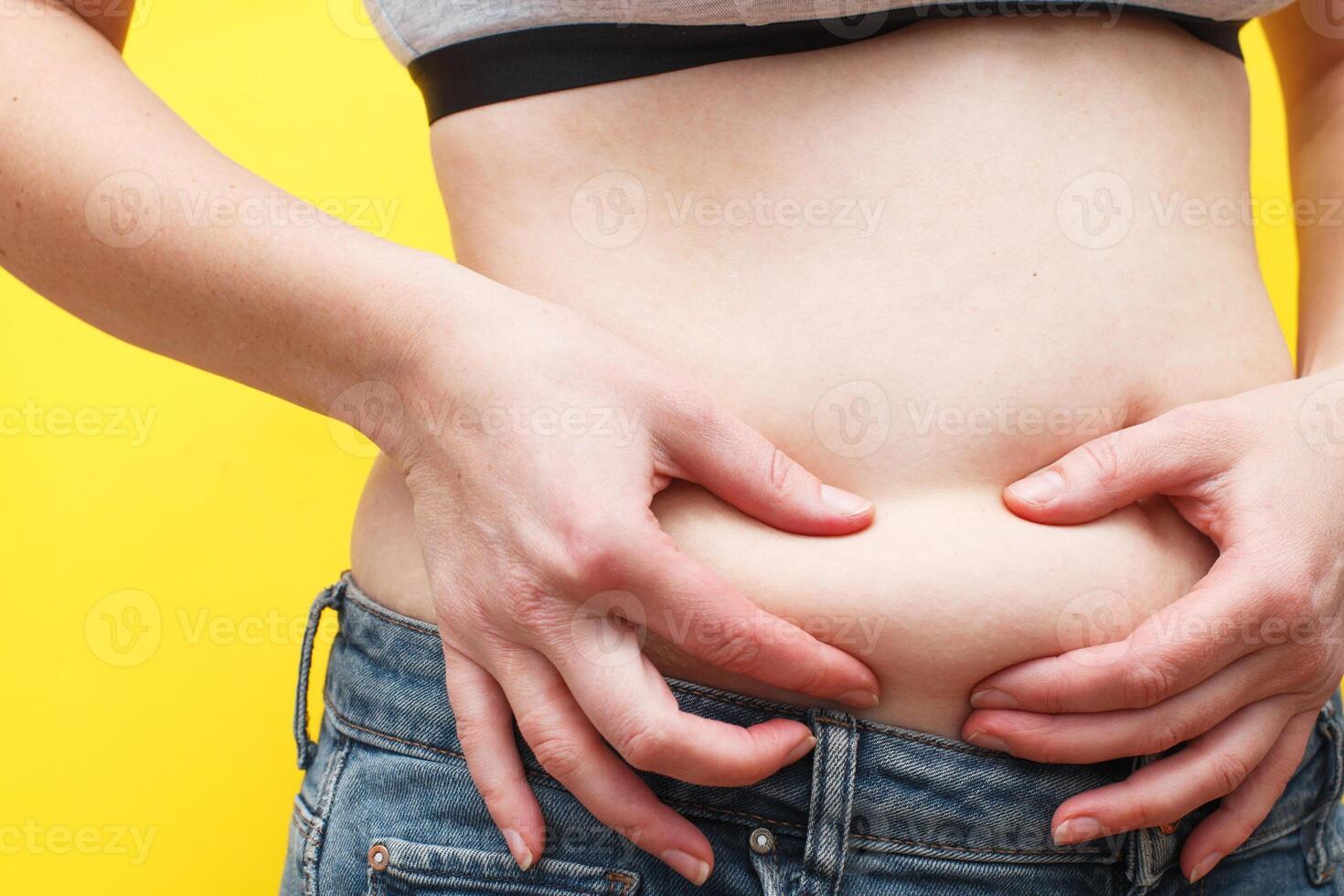 Woman hands compresses the fat on her belly on a yellow background. photo