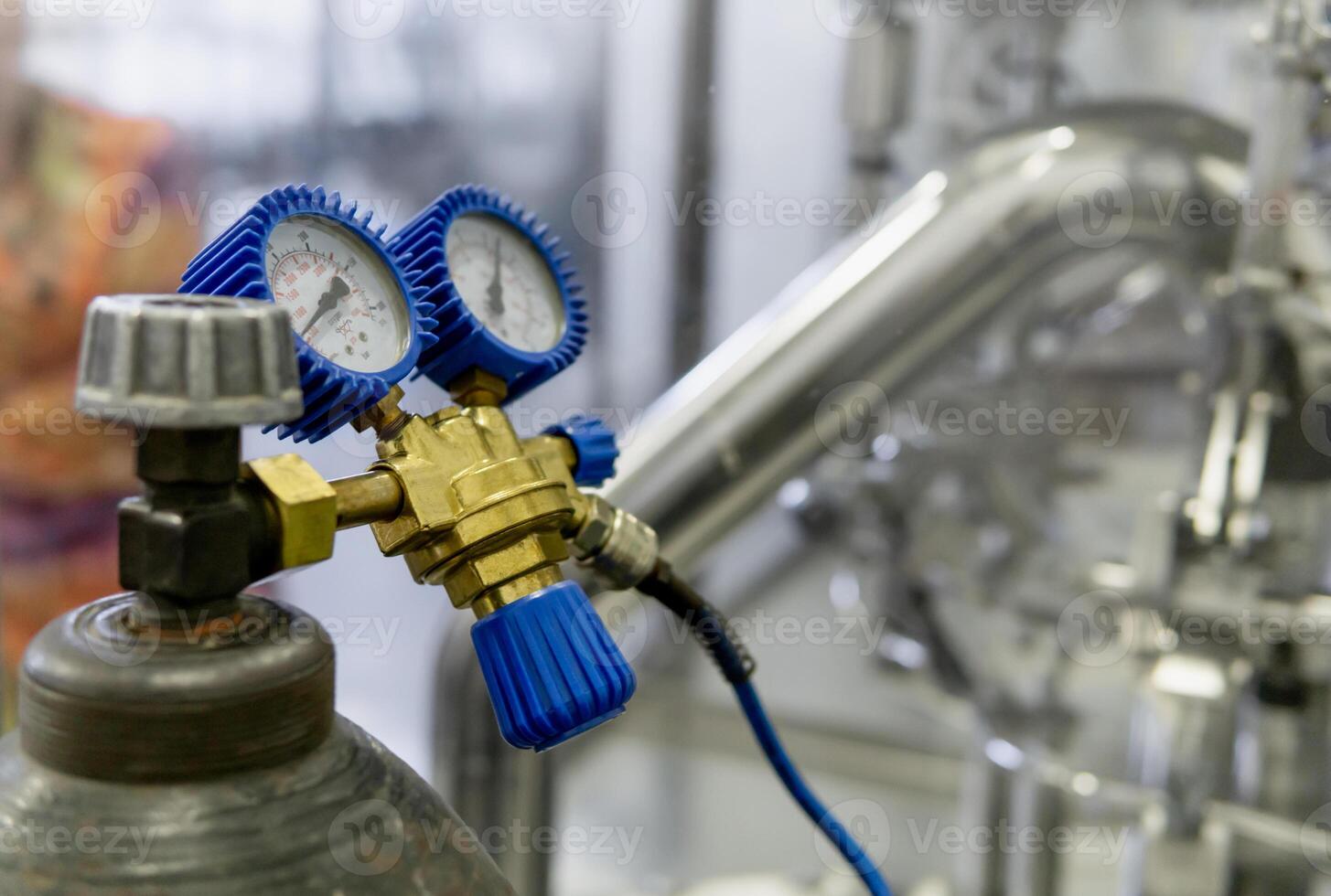 Gas regulator attached to a high pressure cylinder. The regulator has two pressure gauges with blue protective caps to measure the gas pressure inside the cylinder and the outlet pressure. photo