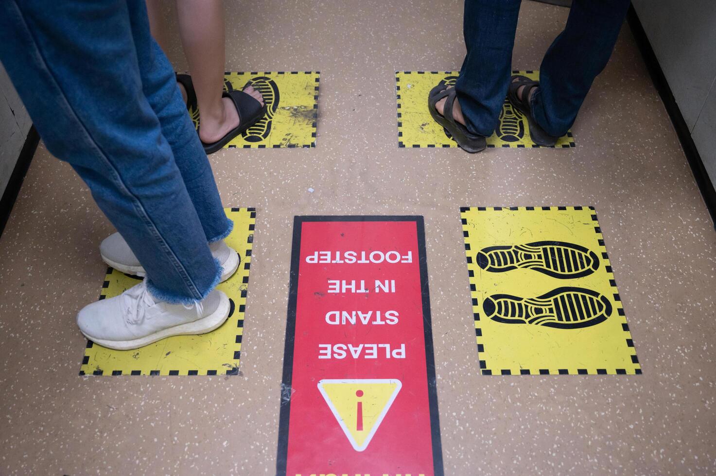 Foot of peoples standing on yellow footprint sign in lift or elevator and keep space for avoid spreading of virus disease in covid-19 pandemic. Social distancing puts space between people. photo