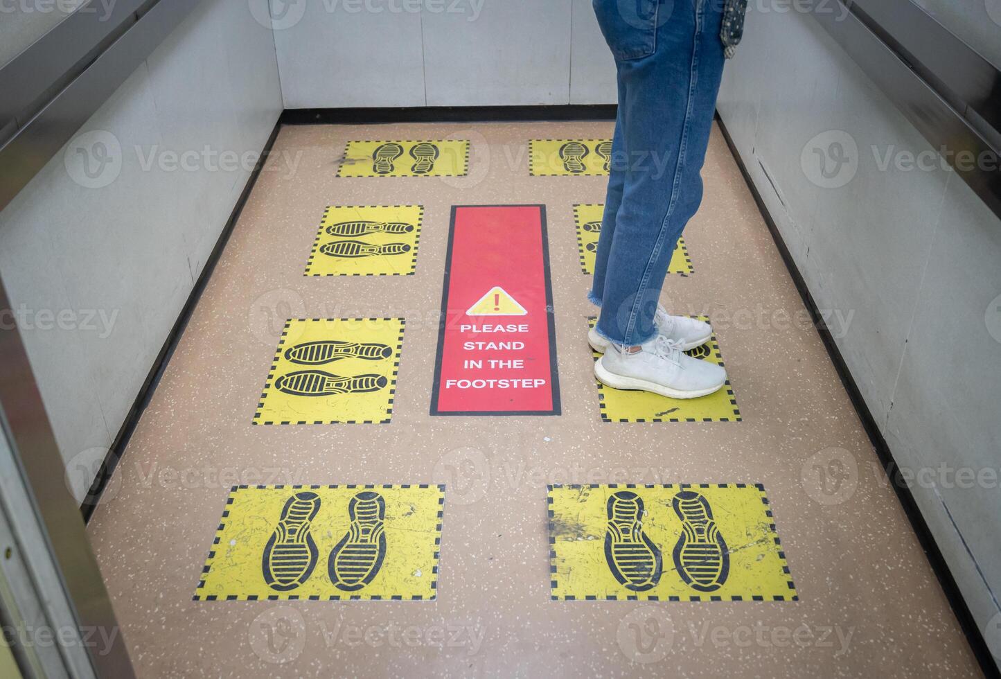 Woman standing on yellow footprint sign in lift or elevator and keep space for avoid spreading of virus disease in covid-19 pandemic. Social distancing puts space between people. photo