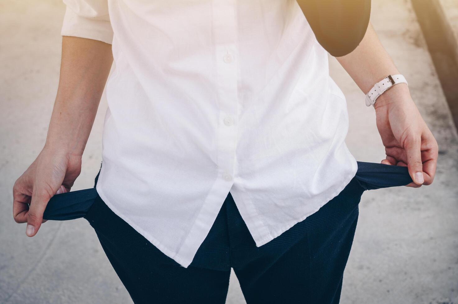 Businesswoman in white shirt turning out and shows empty pockets of her trousers. Conceptual of unemployed woman during Coronavirus recession, economic crisis. photo