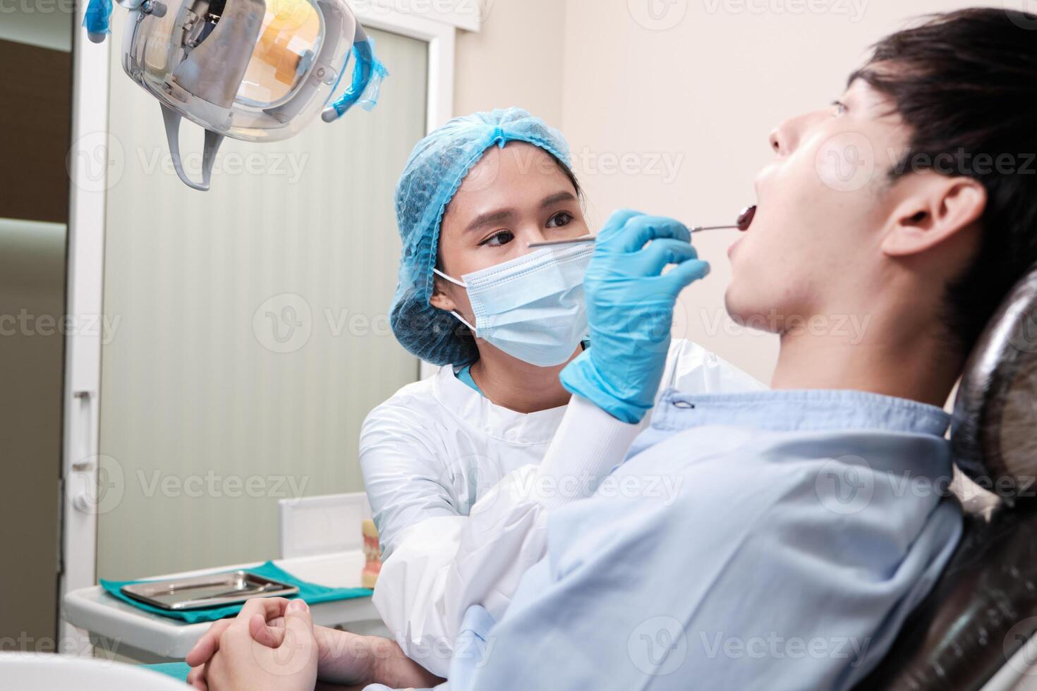 Asian female dentist examine young male patient teeth and toothache stomatology in dental clinic, well-being hygiene checks, and professional orthodontic healthcare work in doctor's office hospital. photo