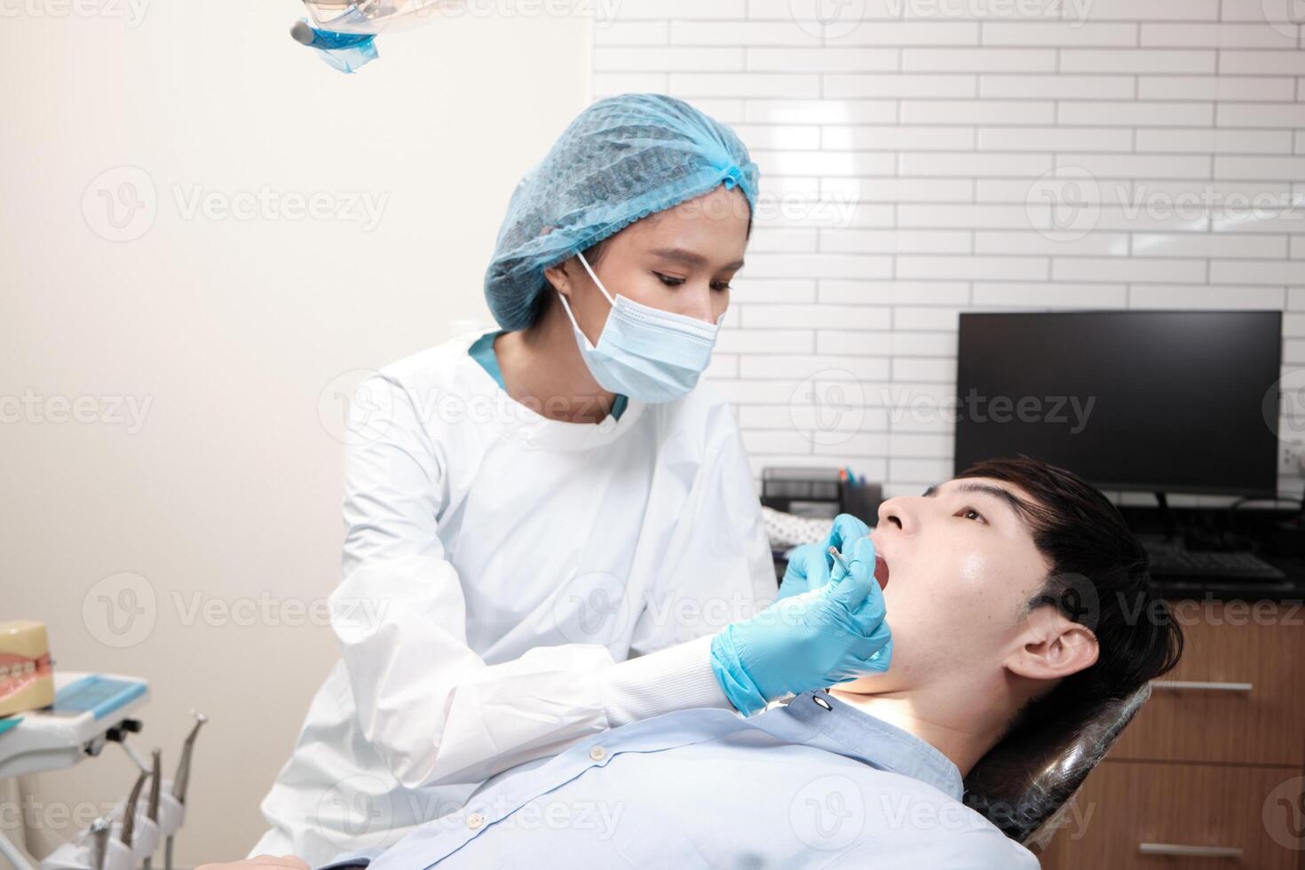 Asian female dentist examine young male patient teeth and toothache stomatology in dental clinic, well-being hygiene checks, and professional orthodontic healthcare work in doctor's office hospital. photo