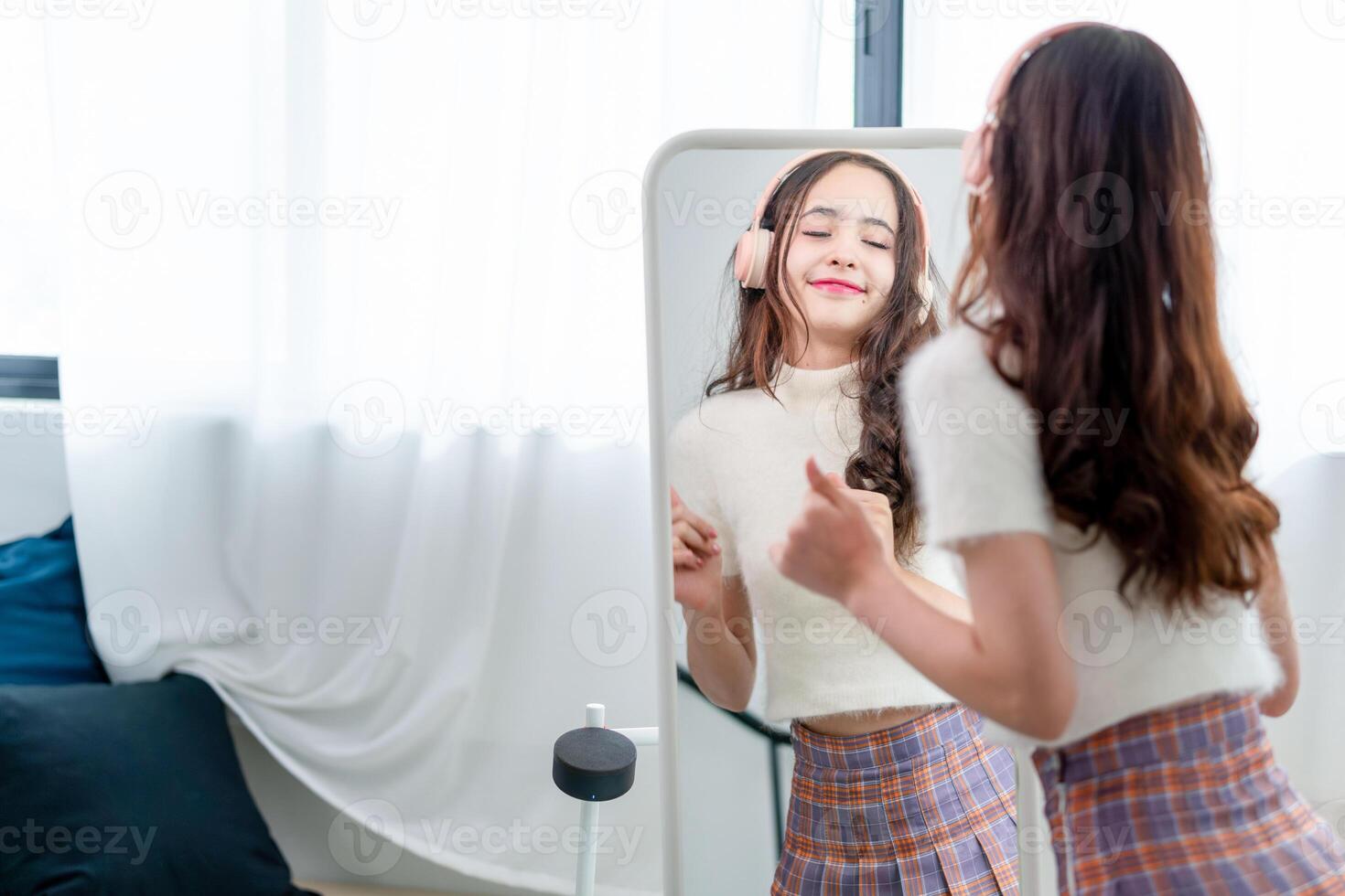Portrait of young girl in headphones listening music and laughing while dancing in front of a mirror in bedroom, Lifestyle at home photo