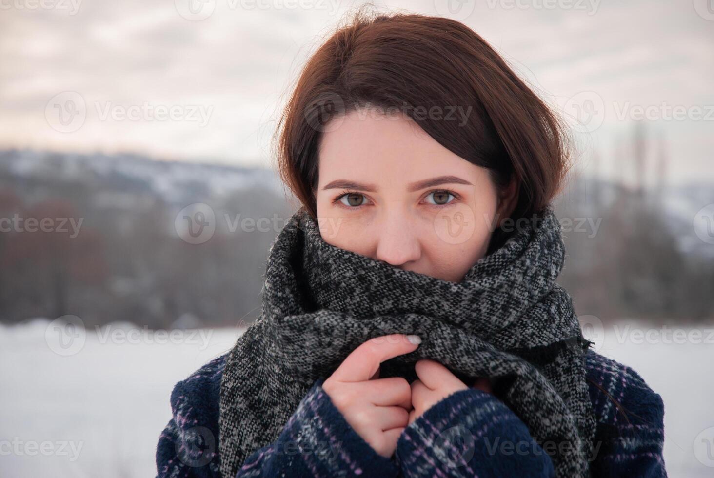 A woman wrapped in a large gray scarf, gazing into the distance with a calm expression, symbolizing warmth and serenity in a winter setting. Captures coziness and reflective moments photo