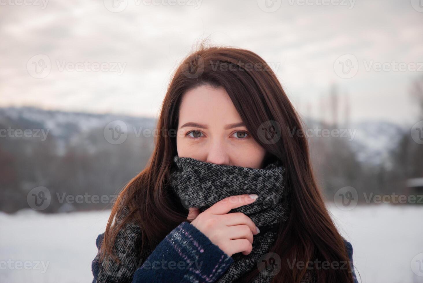 A woman with a large gray scarf covering her face, looking intently into the camera, expressing confidence and mystery. Captures personal style and winter warmth photo