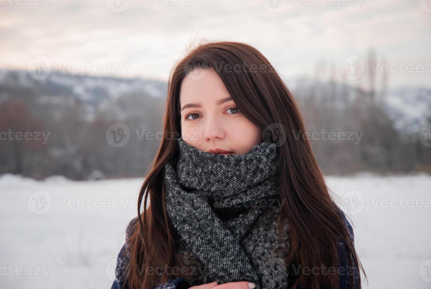 A close-up portrait of a woman wrapped in a plaid coat and thick scarf, gazing calmly into the distance, representing winter warmth and elegance. Highlights personal style and comfort photo