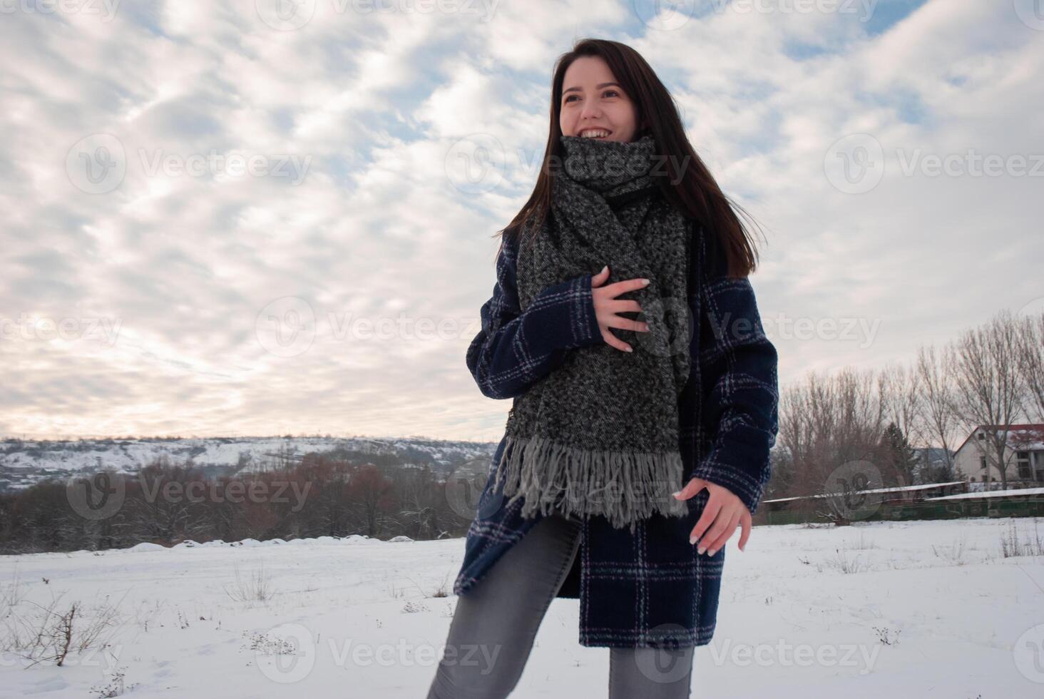 A woman wrapped in a thick scarf and plaid coat, looking over her shoulder with a playful smile, standing in a snowy field. Cozy winter fashion and playful attitude photo
