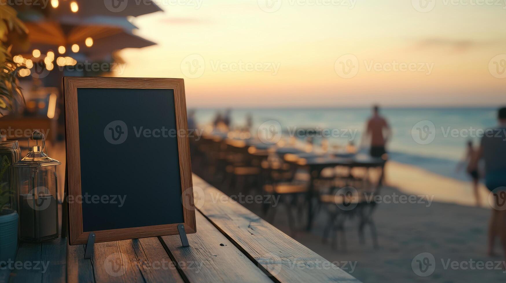 Black blank sandwich board on a wooden deck at a seaside restaurant, with beachgoers and golden sunset in the background. Empty sandwich board photo