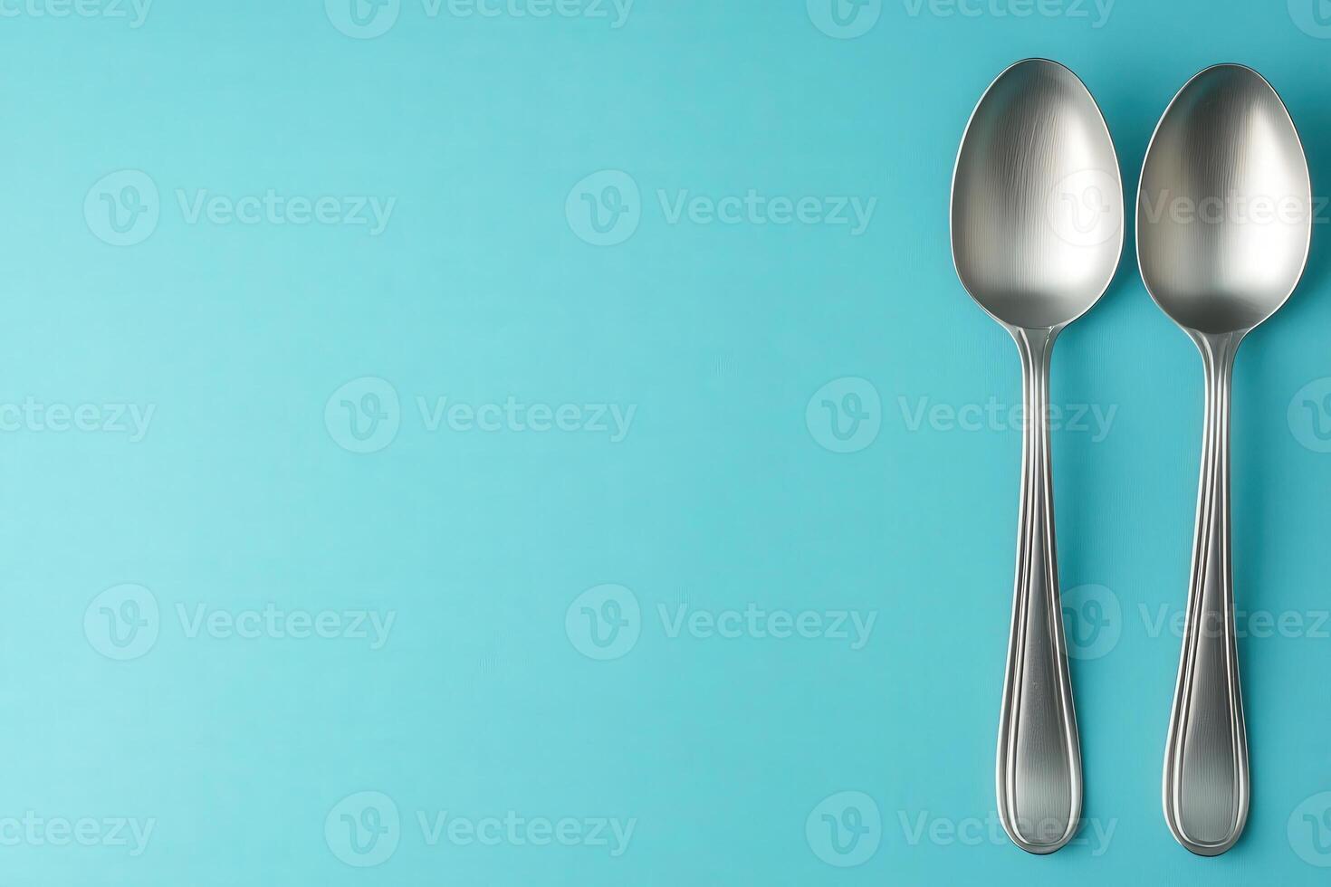 A pair of sleek, metallic spoons sits gracefully on a bright turquoise background, emphasizing the theme of portion control and mindful eating photo