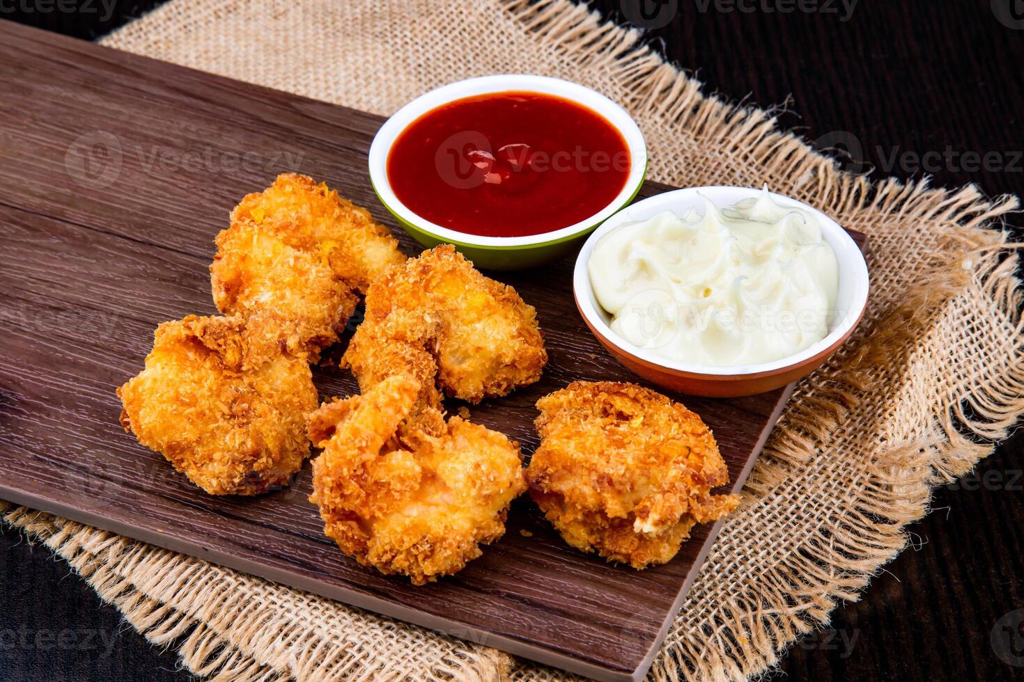 CRISPY COCONUT SHRIMPS with tomato sauce and mayo dip served on wooden board isolated on napkin side view of fast food on dark background photo